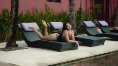 Genç ve güzel Avrupalı esmer kız. Yüzme havuzunun yanında uzanmış. Güneş yatağında.