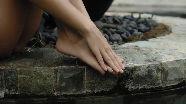 彼女の手で彼女の足に触れる裸足のぬれた足でスイミングプールの近くに座って閉じる水着で若いと美しいヨーロッパの女の子の足 — ストック写真
