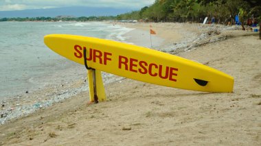 Plajda sarı sörf tahtası ve Bali adasındaki bir sahilde acil durum mesajı.