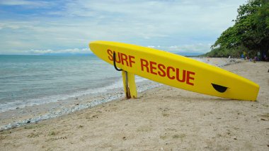 Plajda sarı sörf tahtası ve Bali adasındaki bir sahilde acil durum mesajı.