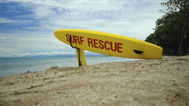 Plajda sarı sörf tahtası ve Bali adasındaki bir sahilde acil durum mesajı.