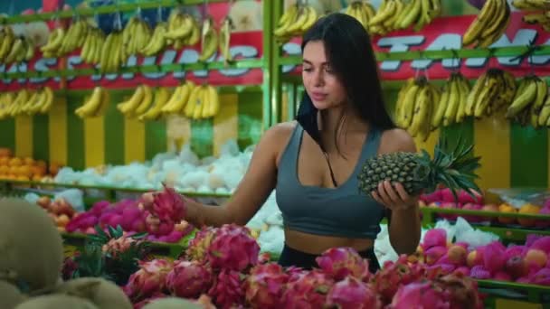 一个年轻的欧洲姑娘在手里拿着菠萝的商店里挑选有机水果 — 图库视频影像