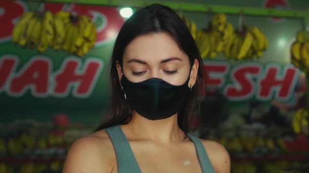一个戴着黑色防护面具的年轻欧洲姑娘在商店里买有机水果 — 图库视频影像