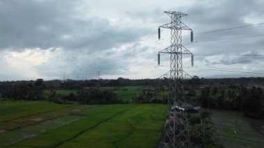 Gün batımında yeşil pirinç tarlasında yeni inşa edilmiş bir elektrik iletim kulesinin hava aracı görüntüsü.
