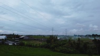 Gün batımında yeşil pirinç tarlasında yeni inşa edilmiş bir elektrik iletim kulesinin hava aracı görüntüsü.
