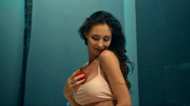 Genç Avrupalı uzun saçlı esmer kız kırmızı çiçeklerle banyoda oturuyor ve spa prosedüründe gül şeklinde sabun kullanıyor.