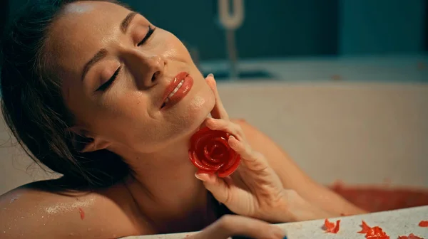 若いですヨーロッパの女の子長い髪のブルネット座っていますバスルームに赤い花とともにAスパプロシージャ上の石鹸でバラの形 — ストック写真