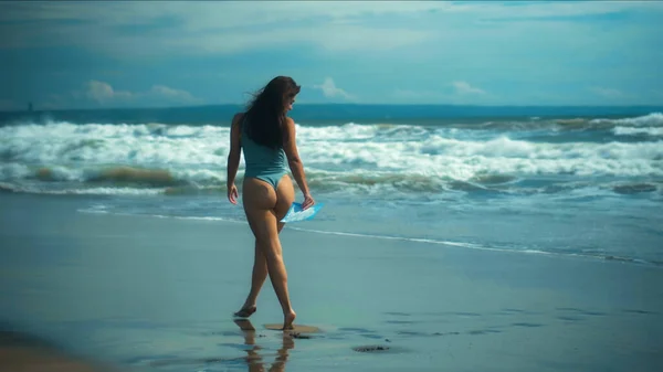 若いですセクシーヨーロッパの女の子でAビキニ歩くと黒砂の上に海によって青い波 — ストック写真