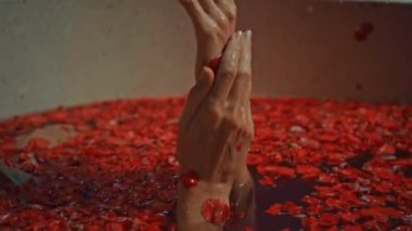 Genç Avrupalı uzun saçlı esmer kız banyoda, spa prosedüründe kırmızı çiçeklerle gül şeklinde sabunla yatıyor.