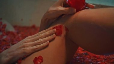 Genç Avrupalı uzun saçlı esmer kız banyoda, spa prosedüründe kırmızı çiçeklerle gül şeklinde sabunla yatıyor.