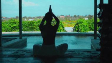 Genç Avrupalı esmer bir kız yeşil tarlalara bakan bir dinlenme odasında havluyla yoga yapıyor.