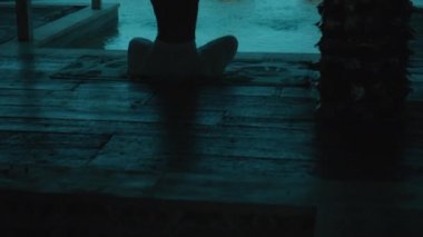 Genç Avrupalı esmer bir kız yeşil tarlalara bakan bir dinlenme odasında havluyla yoga yapıyor.