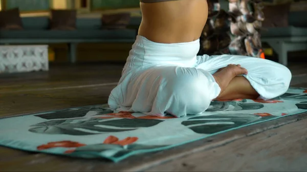 A young European brunette girl sits on a towel and is engaged in yoga in the lounge room