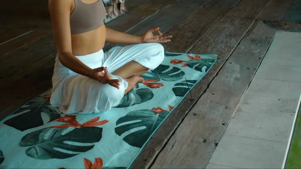 A young European brunette girl sits on a towel and is engaged in yoga in the lounge room