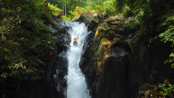 Picture of waterfall with rocks among tropical jungle with green plants and trees and water falling down into the river