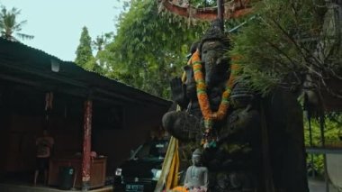 Ganesha 'nın eski taş heykeli, boynunda sarı bir çiçek çelengi olan yosunlarla kaplıydı. Arka planda yeşil bitkilerle sokakta duruyordu.