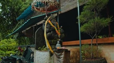 Ganesha 'nın eski taş heykeli, boynunda sarı bir çiçek çelengi olan yosunlarla kaplıydı. Arka planda yeşil bitkilerle sokakta duruyordu.