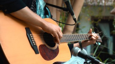 Genç adam, mikrofon kullanarak klasik bir akustik ahşap gitarla el ele oynuyor.