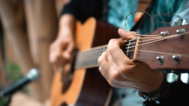 Genç adam, mikrofon kullanarak klasik bir akustik ahşap gitarla el ele oynuyor.