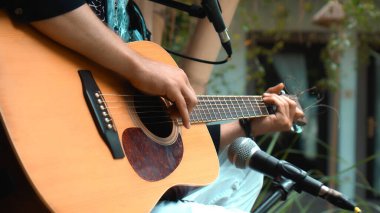 Genç adam, mikrofon kullanarak klasik bir akustik ahşap gitarla el ele oynuyor.