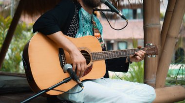 Genç adam, mikrofon kullanarak klasik bir akustik ahşap gitarla el ele oynuyor.