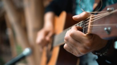 Genç adam, mikrofon kullanarak klasik bir akustik ahşap gitarla el ele oynuyor.