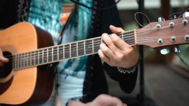 Genç adam, mikrofon kullanarak klasik bir akustik ahşap gitarla el ele oynuyor.