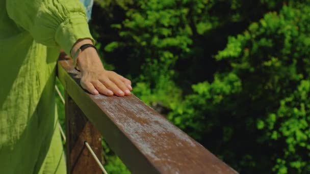一个年轻的欧洲姑娘站在阳台上 手牵着一只穿着绿色连衣裙的木制栏杆 — 图库视频影像