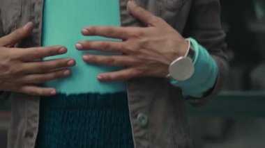 Genç, güzel, Avrupalı, uzun saçlı esmer kız sokakta duruyor ve giysilerine elleriyle dokunuyor.