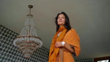 Genç güzel Avrupalı uzun saçlı esmer kız avizenin yanında duruyor ve elleriyle ona dokunuyor.