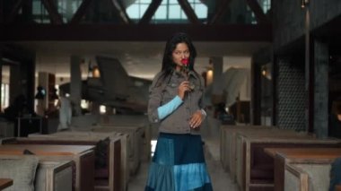 Genç ve güzel bir Avrupalı kız, uzun saçlı bir esmer küçük bir alanda yürüyor ve elinde kırmızı bir gül tutarak kameraya gülümsüyor.