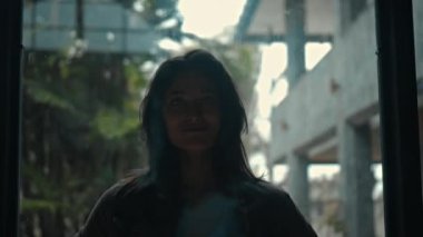 Genç ve güzel Avrupalı uzun saçlı esmer kız karanlıkta pencerenin kenarında duruyor ve gülümsüyor.