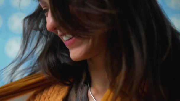 一位年轻貌美的欧洲姑娘 长发黑发 坐在沙发地板上的房间里 凝视着摄像机 微笑着触摸着脖子上的一条黄色围巾 — 图库视频影像