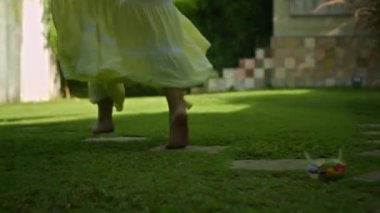 Bahçede çimlerin üzerinde koşan genç bir Avrupalı kızın bacakları. Güzel, sarı bir elbisesi olan yeşil bir bahçe.