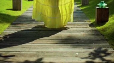 Bahçede çimlerin üzerinde koşan genç bir Avrupalı kızın bacakları. Güzel, sarı bir elbisesi olan yeşil bir bahçe.