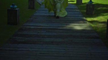 Bahçede yeşil bir bahçe ve çimlerle dolaşan genç bir Avrupalı kız güzel, uzun sarı bir elbise içinde sırtını dönüyor.