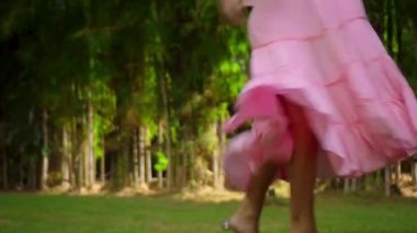 Arka bahçede çimlerin üzerinde dans eden genç Avrupalı bir kızın bacakları. Güzel, pembe bir elbiseyle yeşil bir bahçesi var.