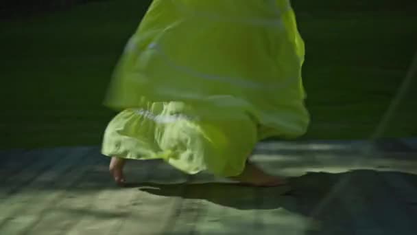 若いヨーロッパの女の子の足は美しい長い黄色のドレスで緑の庭と裏庭の草の中を歩く — ストック動画