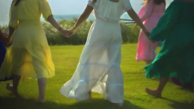 Genç Avrupalı kızlar elbiseli arkadaşlar arka planda yeşil çimlerle birbirlerinin ellerini tutarlar.