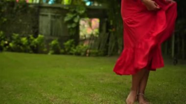 Arka bahçede çimlerin üzerinde dans eden genç Avrupalı bir kızın bacakları. Güzel, uzun kırmızı bir elbise içinde yeşil bir bahçe.