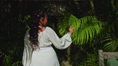 Bahçede yeşil bir bahçe ve çimlerle yürüyen genç bir kız güzel, uzun beyaz bir elbise içinde sırtını dönüyor.