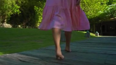 Bahçede yeşil bahçesi ve güzel pembe elbisesi olan çimleriyle dolaşan genç bir Avrupalı kız arkasını dönüyor.