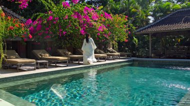 Bahçede yeşil bahçeyle yürüyen uzun saçlı genç bir kız. Mavi temiz suyla dolu bir havuz. Güzel, uzun, beyaz bir elbise. 