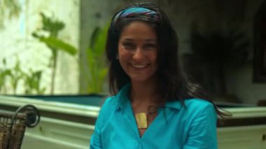 Genç ve güzel Avrupalı uzun saçlı esmer kız arka bahçede mavi giysiler içinde sırıtarak oturuyor.