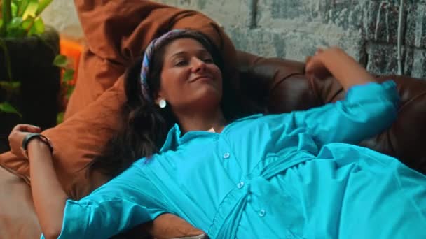 美しいです若いですヨーロッパのブルネットの女の子で青いドレスはソファの上にあり 彼女の手に触れる黄金のリング — ストック動画