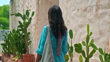 Mavi elbiseli genç bir Avrupalı kız ve elinde bir bayan çantasıyla tropik bölgelerde yeşil bir parkta yürüyor.