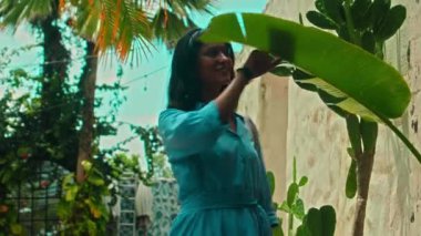 Mavi elbiseli genç bir Avrupalı kız ve elinde bir bayan çantasıyla tropik bölgelerde yeşil bir parkta yürüyor.