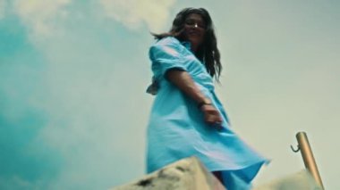 Genç ve güzel Avrupalı bir kız uzun saçlı esmer mavi bir elbise içinde yeşil bitkiler ve beyaz şemsiyelerle caddede yürüyor.