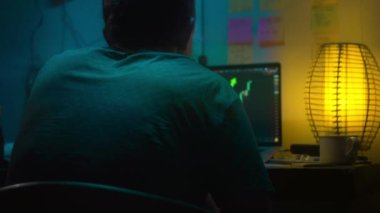 Avrupalı bir kripto tüccarı karanlık bir odada, elinde neon ışığı olan bir dizüstü bilgisayarın arkasında oturur, kripto döviz değişimindeki fiyat hareketlerinin grafiklerini gösteren bir ekrana bakar. Bir sigara içiyor. Bulanık arkaplan
