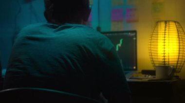 Avrupalı bir kripto tüccarı karanlık bir odada, elinde neon ışığı olan bir dizüstü bilgisayarın arkasında oturur, kripto döviz değişimindeki fiyat hareketlerinin grafiklerini gösteren bir ekrana bakar. Bir sigara içiyor. Bulanık arkaplan